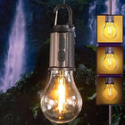A hanging lantern-style light bulb with a visible glowing filament and built-in switch, shown against a dark waterfall background. Three inset panels on the right show the bulb glowing in different warm light tones.