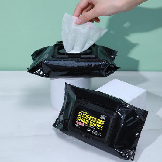 Hand pulling a shoe shine wipe from a black packaging with 'Shoe Shine Wipes' text.