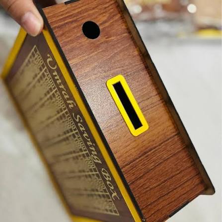 Wooden savings box with yellow label held by a hand on a blurred background